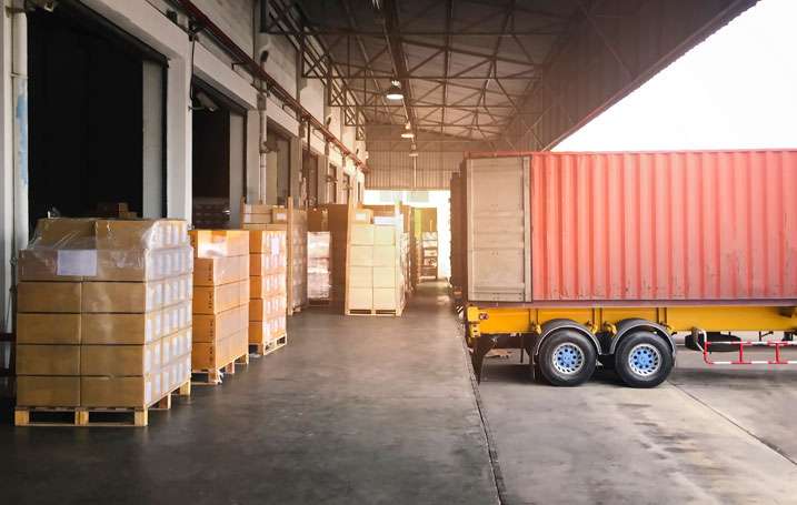 Delivery truck unloading large shipment of pallets with boxes at New Hampshire warehouse loading dock